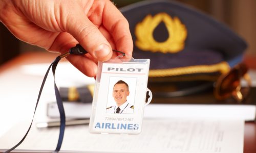 Hand with professional airline pilot id holder, hat sun glasses laying on log book and flight plan in background